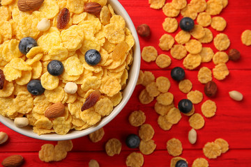 Bowl with cornflakes, nuts, raisins and blueberry on red wooden background