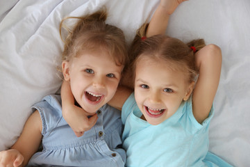 Adorable little sisters lying in bed, top view