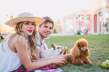 Young attractive couple resting in the park on the green lawn with dog and rabbit
