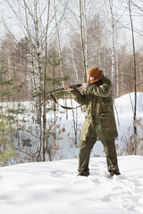 Hunter man with old 16 caliber side-by-side double-barreled shotgun dressed in camouflage clothing in the winter forest