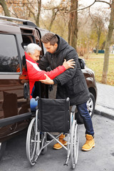 Young man helping handicapped man to sit in wheelchair