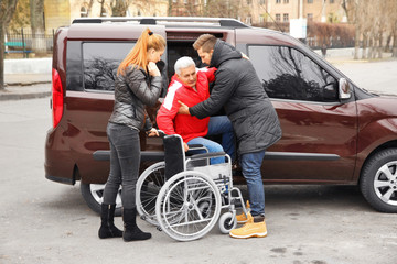 Obraz premium Young couple helping handicapped man to sit in wheelchair