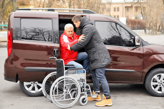 Young Man Helping Handicapped Man To Sit In Wheelchair