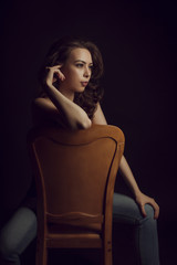 Charming topless woman in blue jeans sitting on a chair