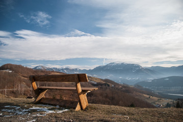 Isolated wooden bench on the edge of the cliff towards the mountains covered in snow 