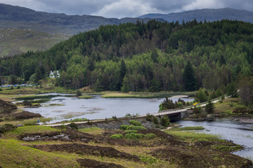 Northwest Coast, Scotland - June 6, 2012: The road bridges a narrow point of Loch Dubhaird Mor north of Kylesku. Green forested hills, high bare mountains, flowing water. Semi aerial view.
