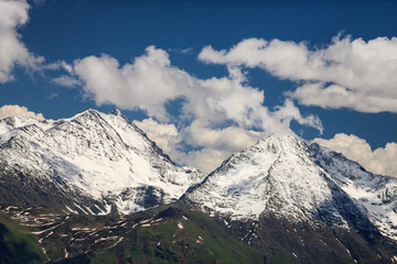 Beautiful scenic landscape of snow covered mountain peaks in Caucasus mountains at spring on a sunny day with blue sky and white clouds