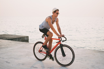Fototapeta na wymiar Young man with his fixed gear bike on seafront during sunset or sunrise