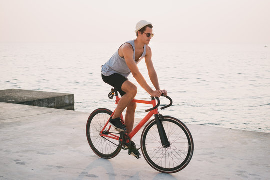 Young man with his fixed gear bike on seafront during sunset or sunrise