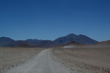 Fototapeta na wymiar Dirt road heading into the distance across the dusty remote desert and Altiplano region of South West Bolivia