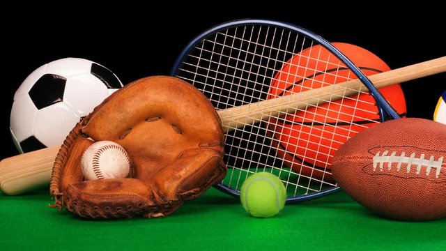 Pan of sports equipment including a basketball, baseball gear, a tennis racquet, soccer ball and volleyball against a black background.