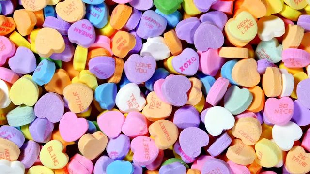 A rotating bowl of sweet Valentines heart shaped candy in various pastel colors and messages of affection..