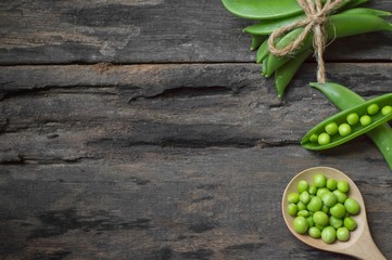 Green peas in wooden spoon on old wooden background