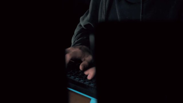 Male hand of hacker in hood typing crack code using computers in dark room