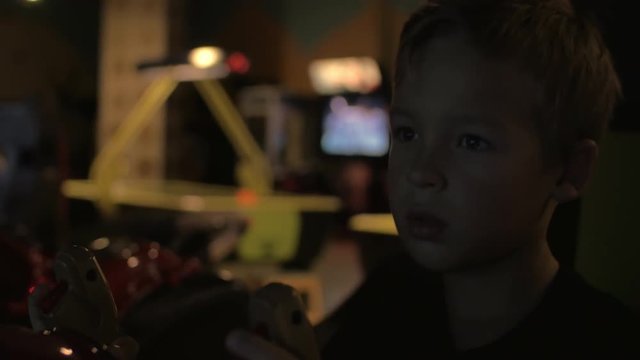 Close up view of boring tired small boy are playing video arcade game in game center against flashed screen