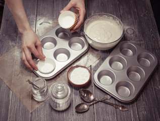 Female hands prepare molds for home-made cupcakes. Home-made pastries. Soft vintage toning