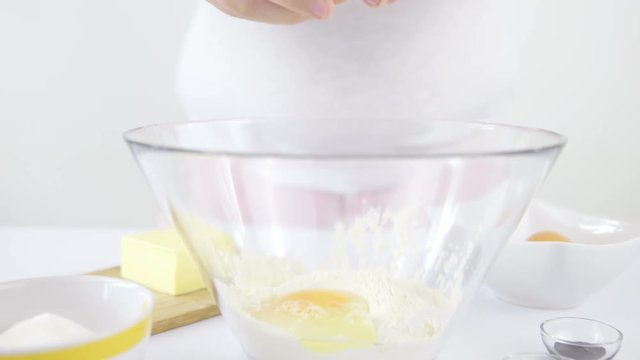 Person breaking egg inside glass bowl with flour 4K