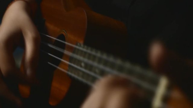 Somebody playing ukulele in close up view. Shift focus to finger.