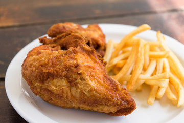 Fried chicken breast with potato chips on a white plate on a wooden table.