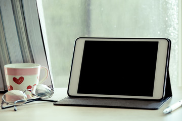 Fototapeta premium Digital tablet on table in the workplace on rainy day window 