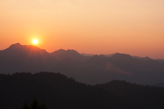 Sun shining through silhouetted mountains.