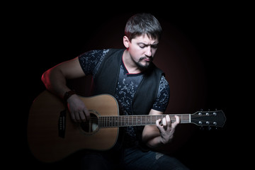 Obraz premium Portrait of a young bearded guitarist clamping chord on an acoustic guitar on a black background