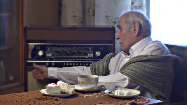 Grandad Setting Radiogram in Lunch Time Tea Cup Cake Piece on the Table in Cosy Living Room Cold Wintry Day at Home Vintage Interior Comfortable Armchair