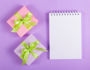 Open notebook with a blank page and two gift boxes on a purple background. Copy space. Holiday concept.