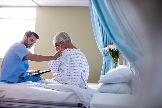Male doctor consoling a senior patient on bed