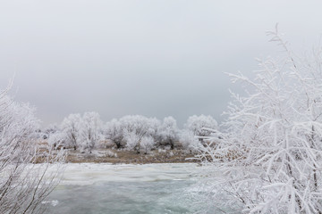 Beautiful winter scenery with trees covered by frost, along frozen river, and storm clouds