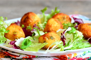 Fried potato balls with salad leaf mix and basil on a plate. Small golden fried balls made from mashed potatoes, eggs, flour, salt and pumpkin seeds. Vegetarian dish. Closeup