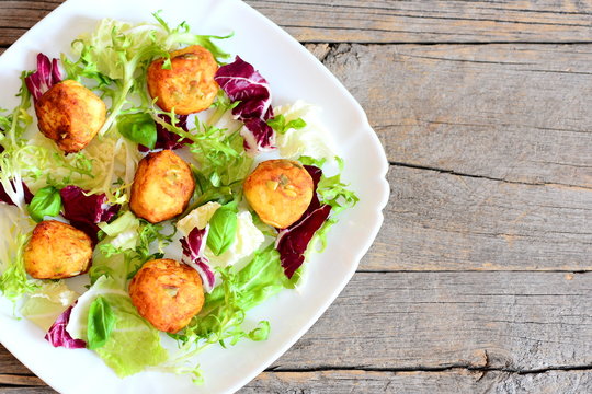 Fried potato balls recipe. Homemade fried mashed potato balls with pumpkin seeds served with fresh lettuce and basil. Wooden background with copy space for text. Top view