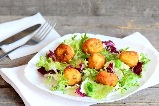 Crispy fried potato balls recipe. Home fried mashed potato balls with pumpkin seeds served with fresh lettuce and basil on a plate. Cutlery, napkin on vintage wooden table