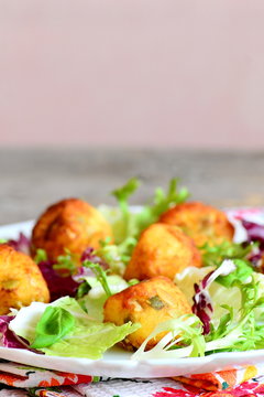 Fried mashed potato balls with salad leaf mix and basil on a plate. Small fried balls made from mashed potatoes, eggs, flour, salt and pumpkin seeds. Vertical photo