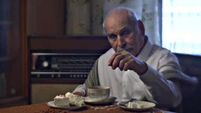 Old Man is Mixing Sugar in a Tea Has Breakfast Sitting at the Table in Cosy Living Room Vintage Radiogram in Behind Cold Wintry Day at Home Nostalgia