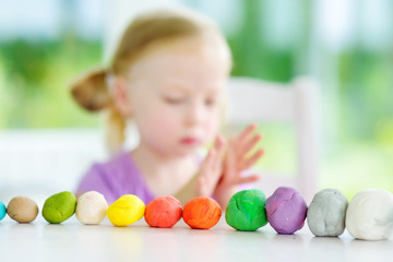 Fototapeta na wymiar Cute little girl having fun with modeling clay at a daycare. Creative kid molding at home.