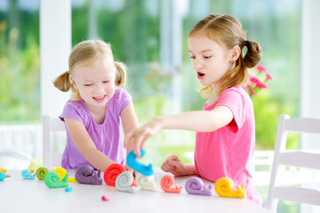 Obraz na płótnie Canvas Two cute little sisters having fun together with modeling clay at a daycare. Creative kids molding at home. Children play with plasticine or dough.