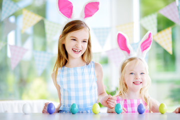 Fototapeta na wymiar Two cute little sisters wearing bunny ears playing egg hunt on Easter