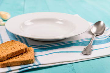 Empty White Plate With Blue Napkin And Spoon On Table