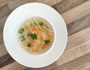 Top view of chicken bouillon with carrot, celery and parsley. Chicken broth on wooden background.