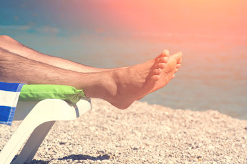 Men's feet on a lounger near the sea in the sunlight