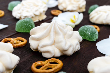 Sweets: meringues and jelly hearts, white orchid flowers, salty Bretzel on a dark wooden board.Close up