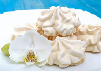 Light air vanilla meringue on a white plate with orchid flower on a blue background. Close-up.