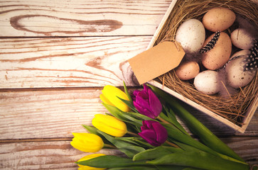 Fototapeta na wymiar Easter background with eggs in nest and purple and yellow tulips. Top view with copy space