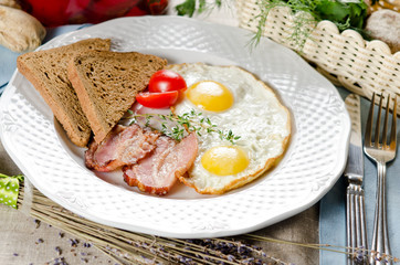 Hearty breakfast. Fried eggs with bacon, rye bread and cherry to
