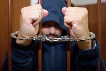 Abstract. Hands of the prisoner on a steel lattice close up. Prison, man in handcuffs.