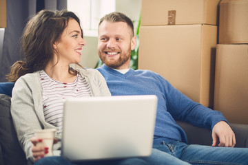 couple in new apartment using laptop. Lot of moving boxes around them