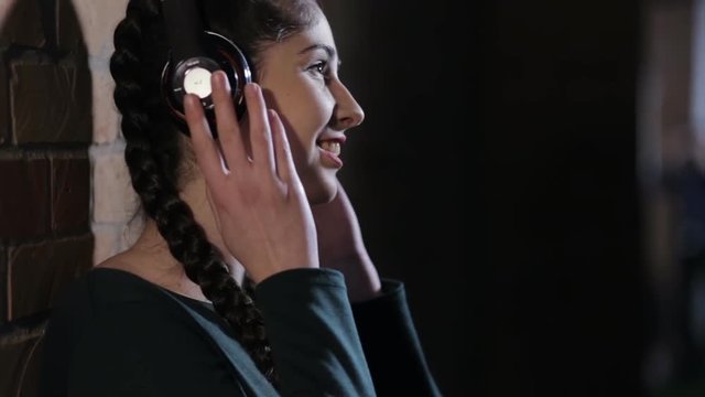 Woman in earphones listen music at brick wall in dark room