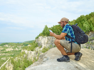 Man tourist uses tablet computer sitting on edge of cliff in mou