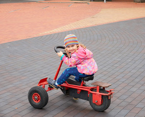 Little girl having fun driving a pedal car in day.
